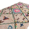cream-wool-moroccan-rug-with-colorful-motifs Front-facing image of a cream Berber rug featuring multicolor geometric motifs and green lattice lines.