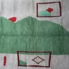 handmade-berber-rug-cream-green-design Close-up view of the rug’s textured wool surface highlighting the green abstract shape and red details.