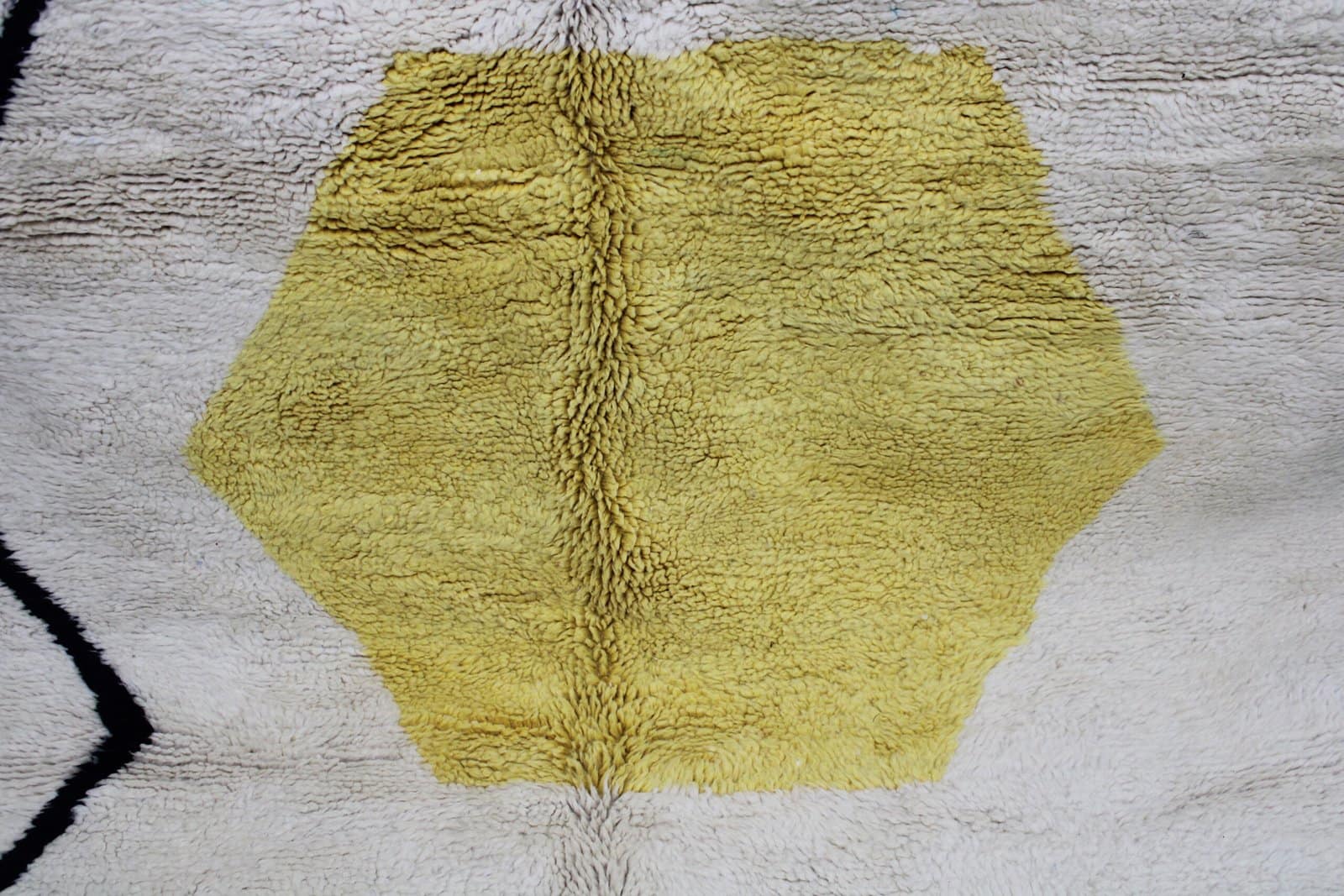 luxury-berber-wool-rug-minimalist Close-up of Moroccan wool rug texture showing cream pile and yellow geometric shape.