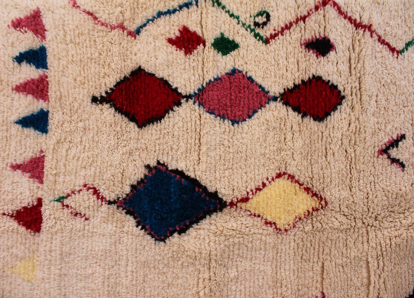 modern-boho-moroccan-carpet Detailed view of red, blue, green, and pink tribal symbols on handmade Moroccan rug.