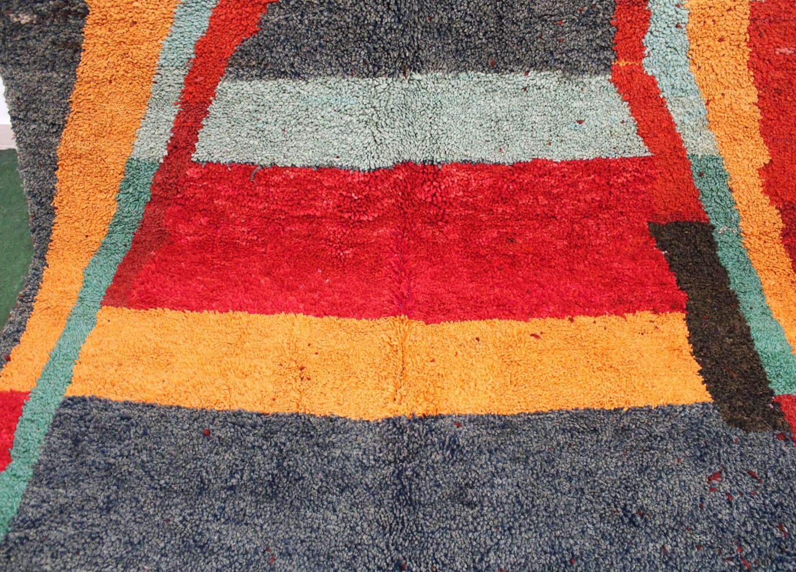 authentic-moroccan-tribal-shag-carpet Center close-up displaying large arch-inspired motif in red and green on dark background.