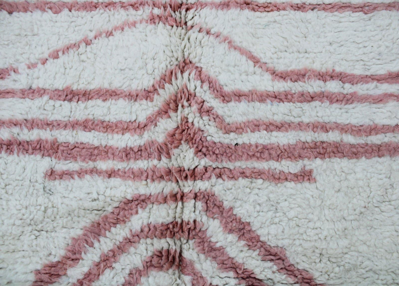berber-chevron-handwoven-rug A close-up of a brown and regabé wool rug with a distinctive pattern and light pink and cream tones.