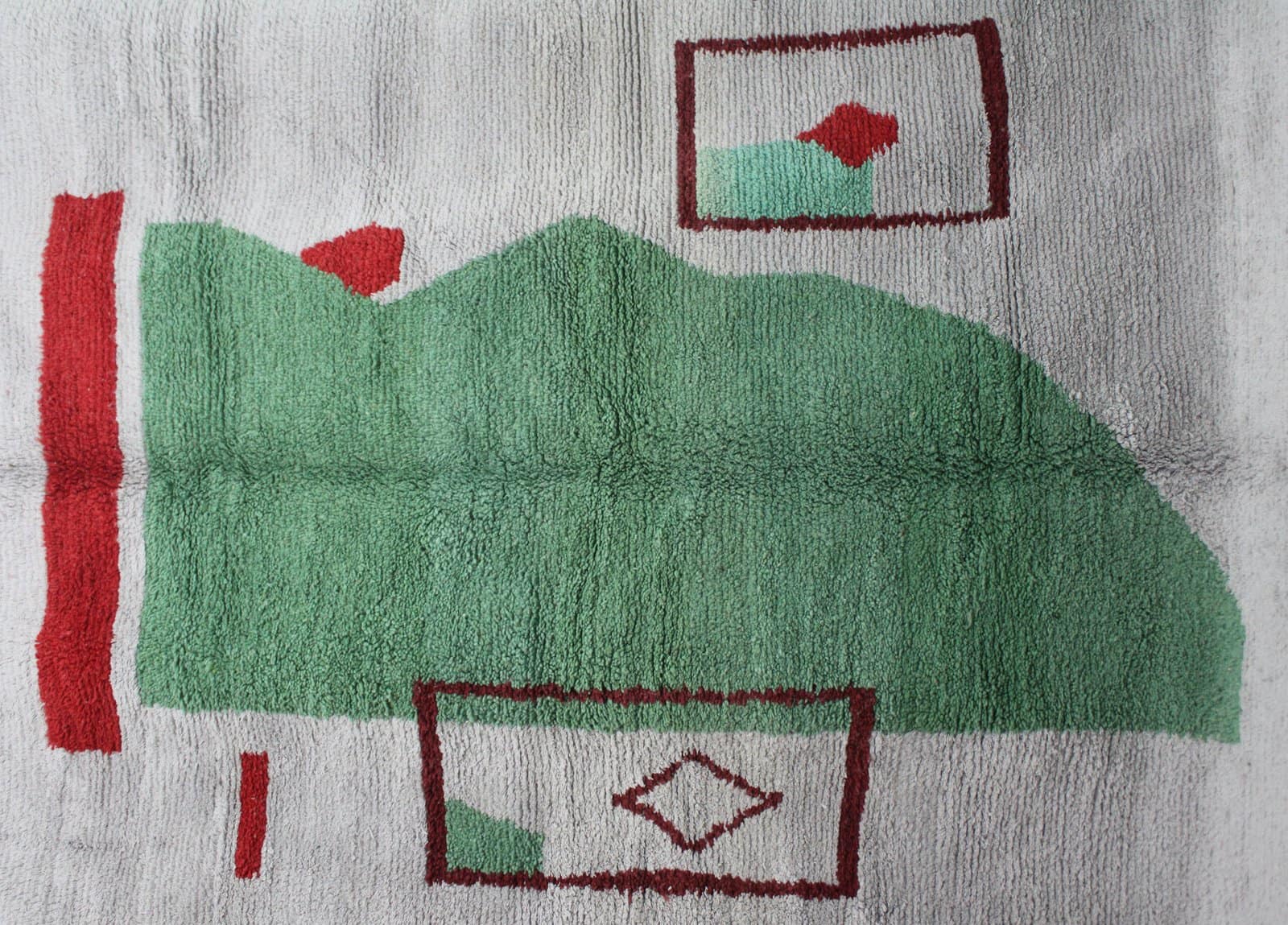 handmade-berber-rug-cream-green-design Close-up view of the rug’s textured wool surface highlighting the green abstract shape and red details.