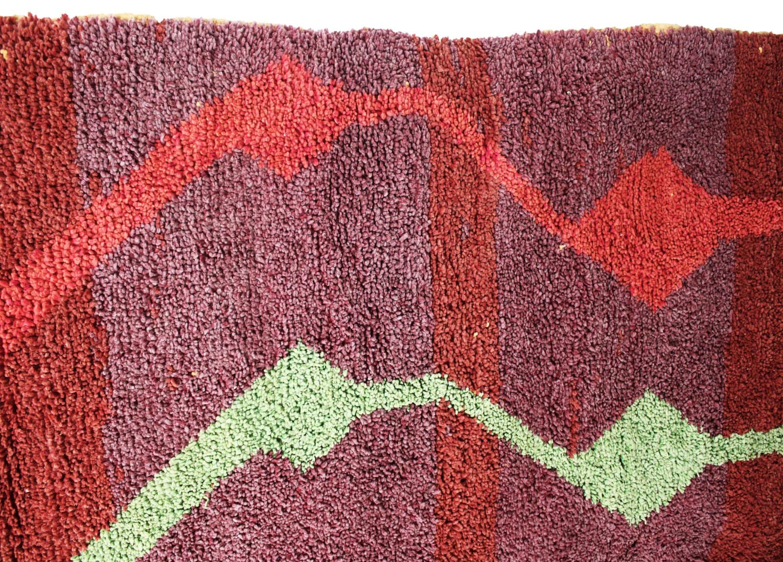 red-beni-ourain-style-rug-geometric-pattern Side angle view of the Moroccan Berber rug highlighting its thickness and handwoven texture.